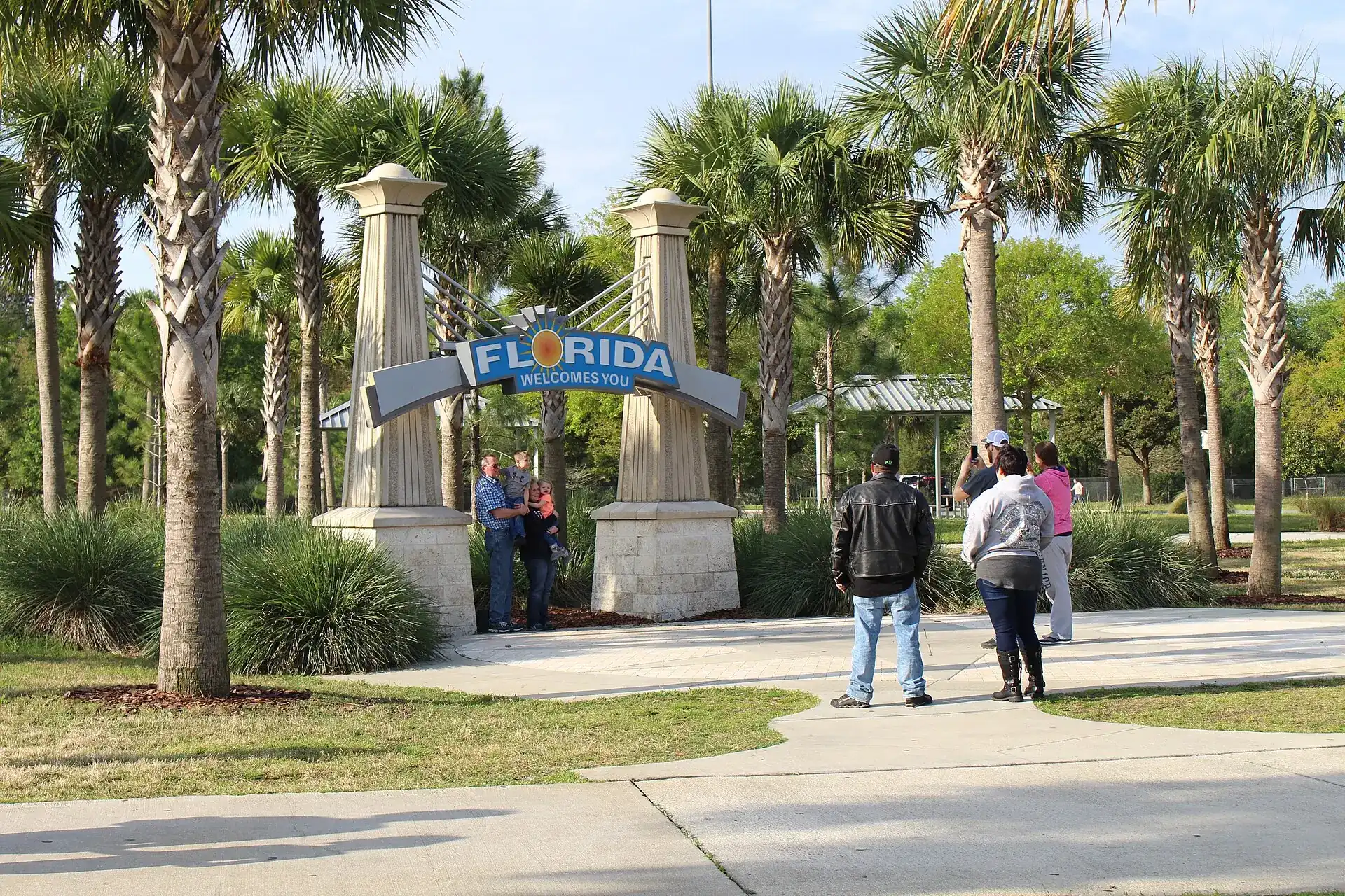 Visitors arriving beneath a Florida welcome sign framed by palm trees
